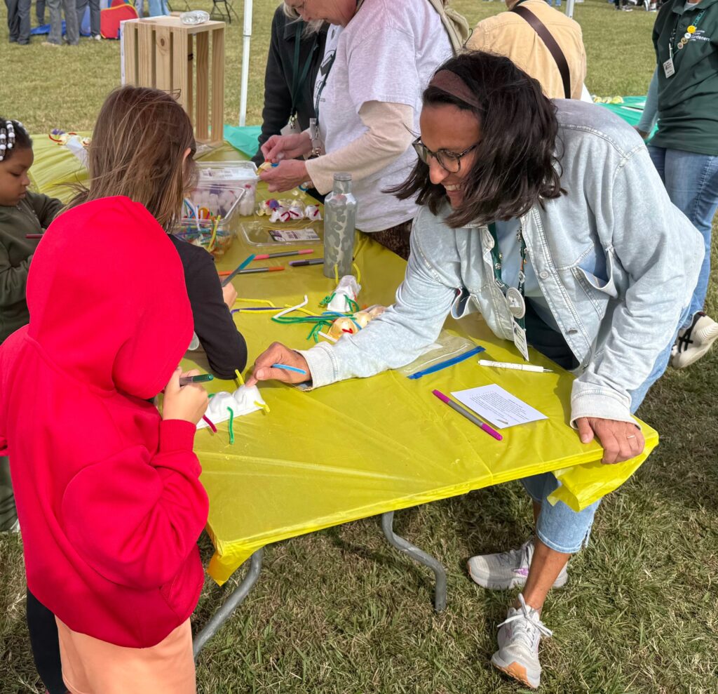 Person helping a child make a caterpillar out of styrofoam egg cartons.